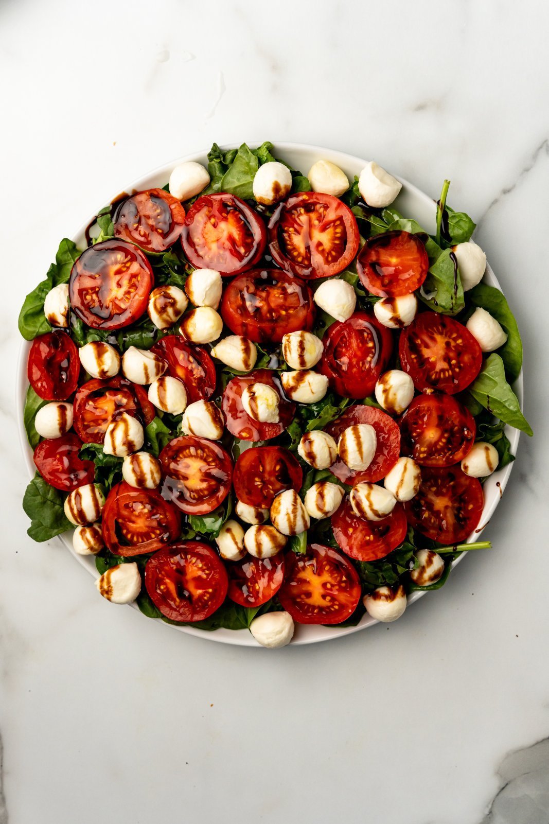 a large plate with spinach tomatoes and boccicini topped with balsamic glaze and olive oil