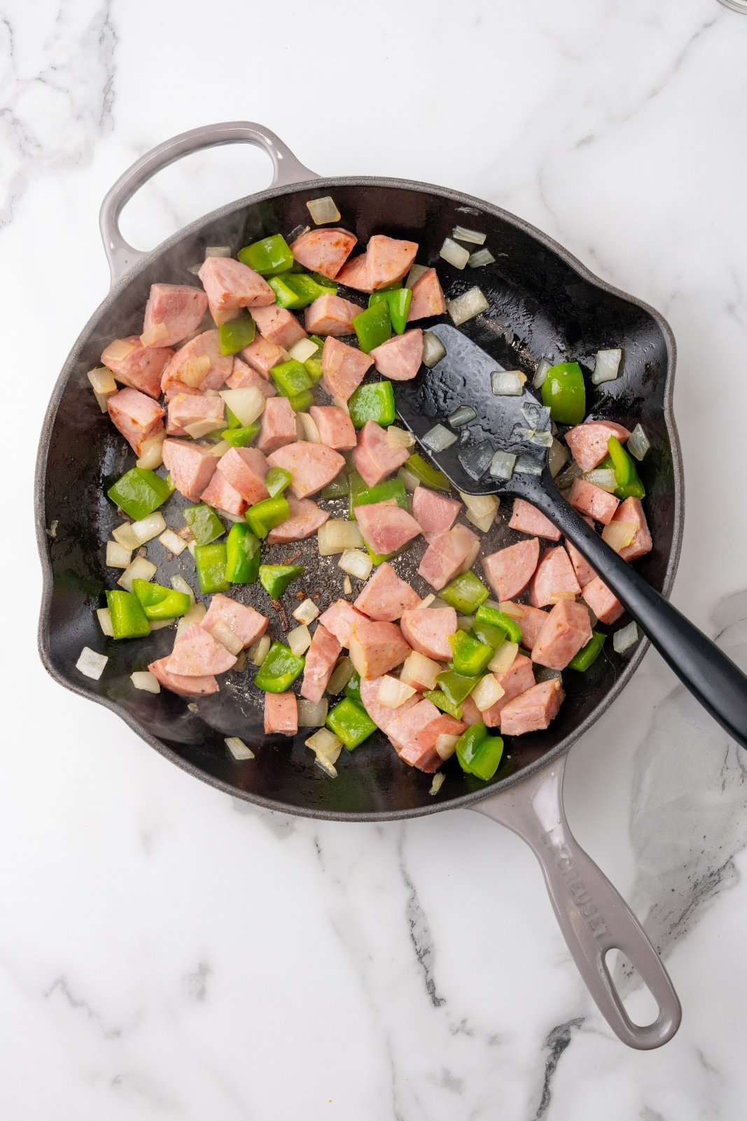 Kielbasa, green pepeprs and onions in a skillet cooking