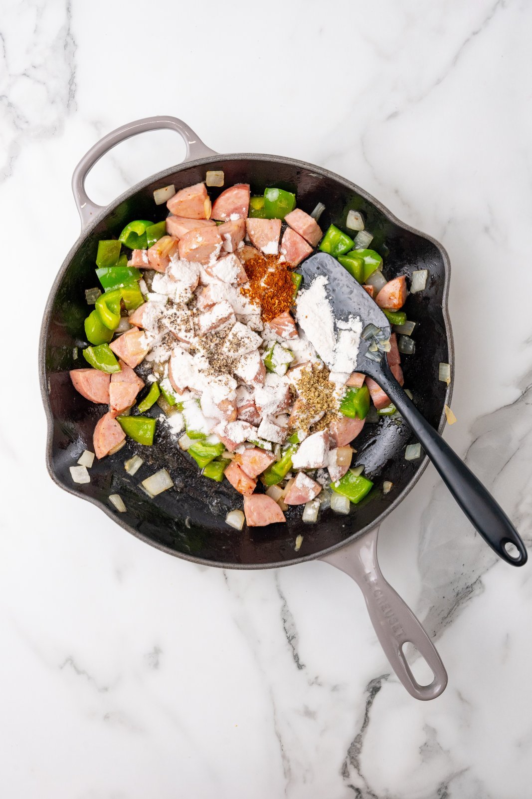Kielbasa, green pepeprs and onions in a skillet cooking with seasonings on top