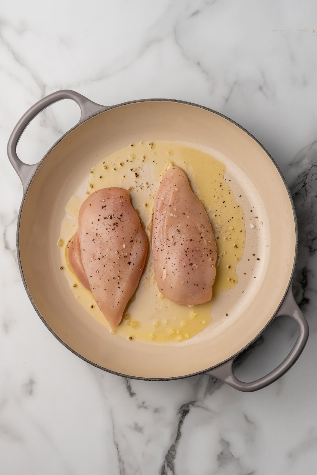 2 chicken breasts added to a pan with oil, seasoned with salt and pepper