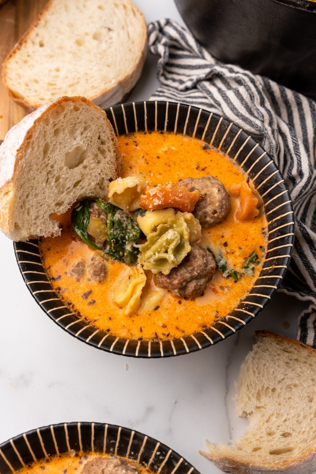 a bowl of cremay tortellini meatball soup with bread being dipped in