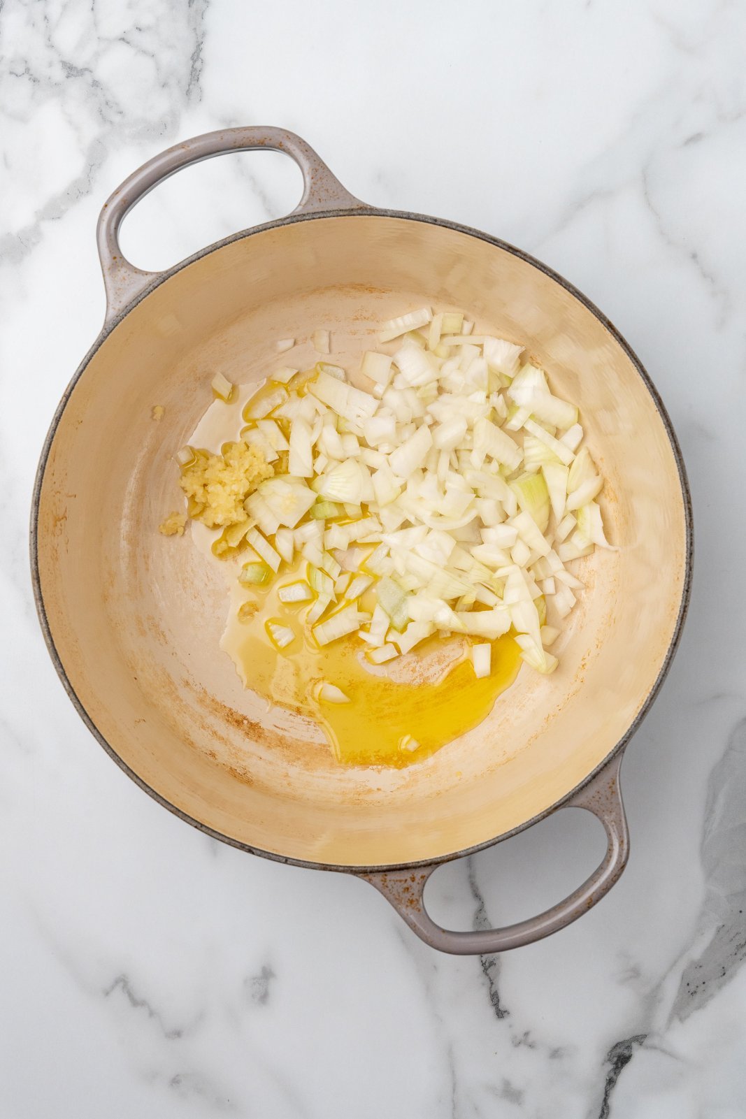 olive oil onion and garlic before cooking in the bottom of a large grey dutch oven pot