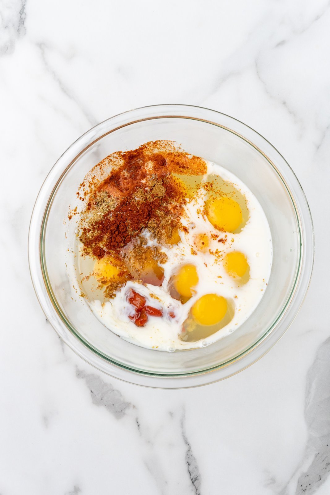 a glass bowl with eggs, milk, salsa,seasonings