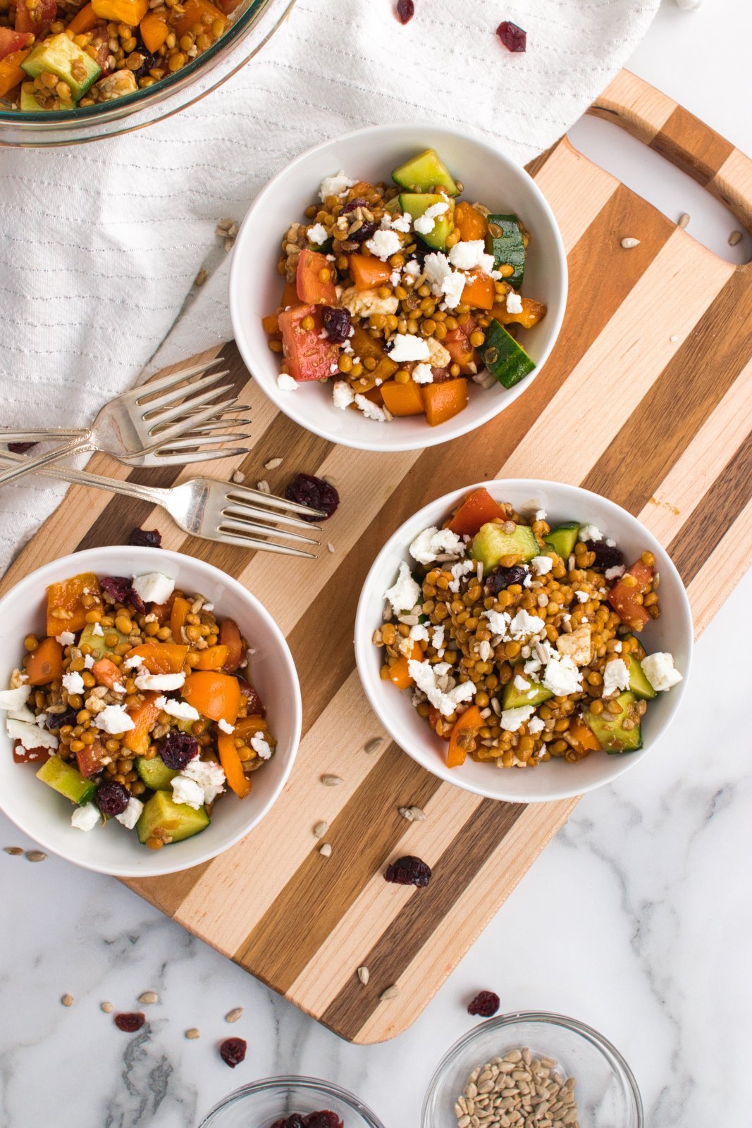three bowls of lentil feta salad on a cutting board