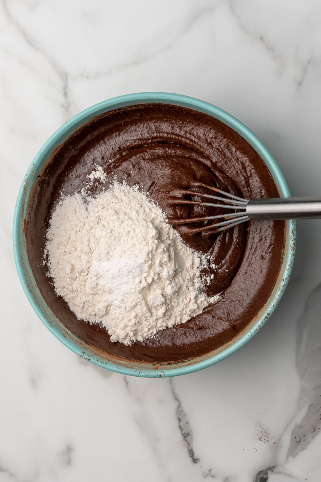 the brownie batter with flour, baking powder and salt on top with a whisk in the bowl