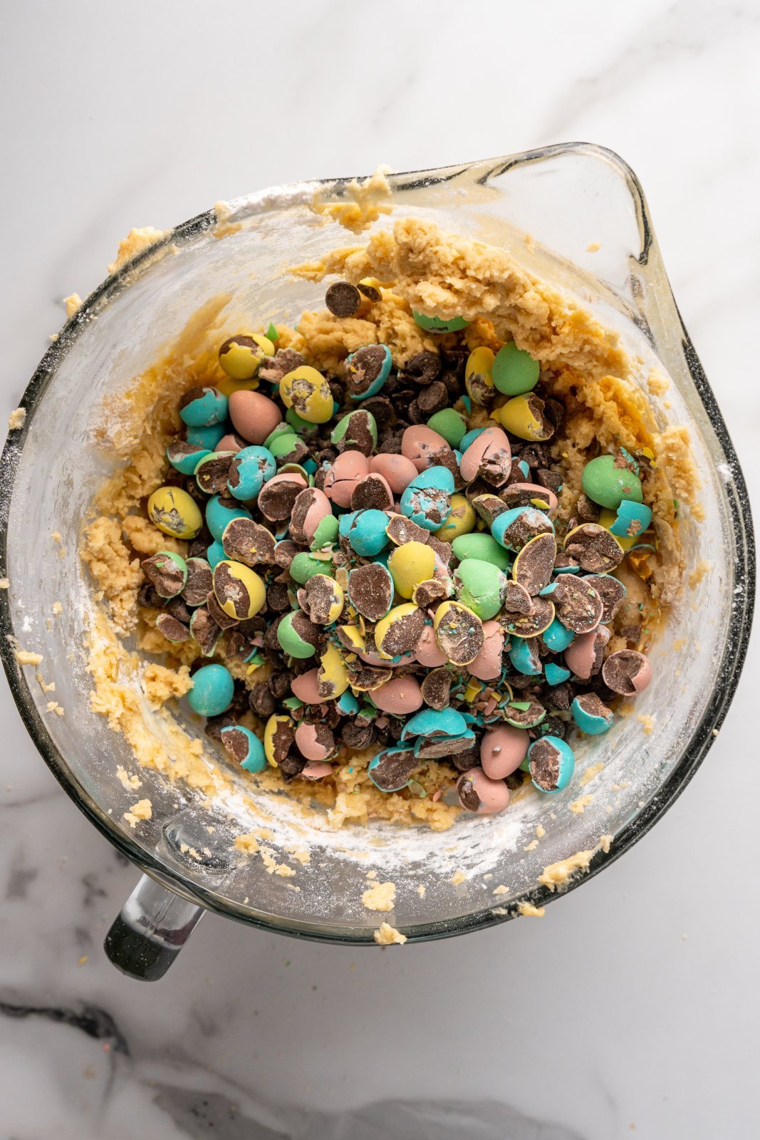 a bowl of cookie dough with mini eggs and chocolate chips waiting to get mixed in