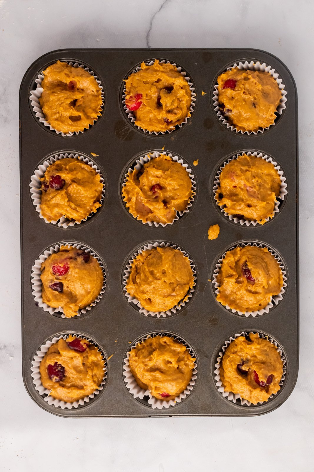 12 raw pumpkin cranberry muffins in the tin are shown