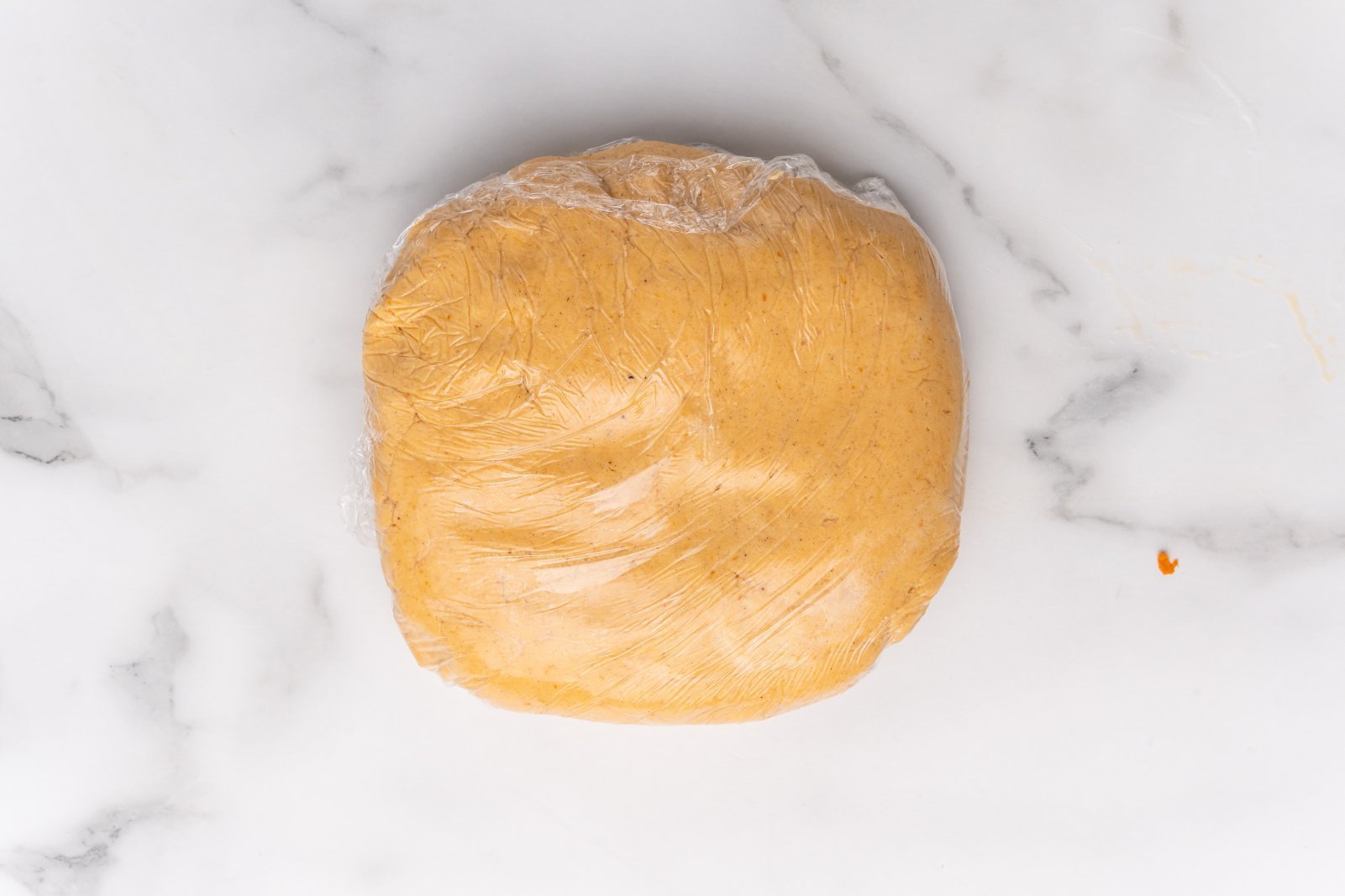 pumpkin sugar cookie dough flattened into a disk and saran wrapped