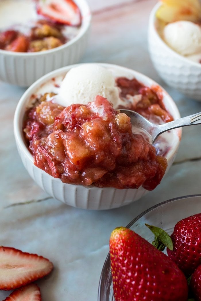 apple strawberry crumble overflows from a bowl and has a scoop of ice cream on top