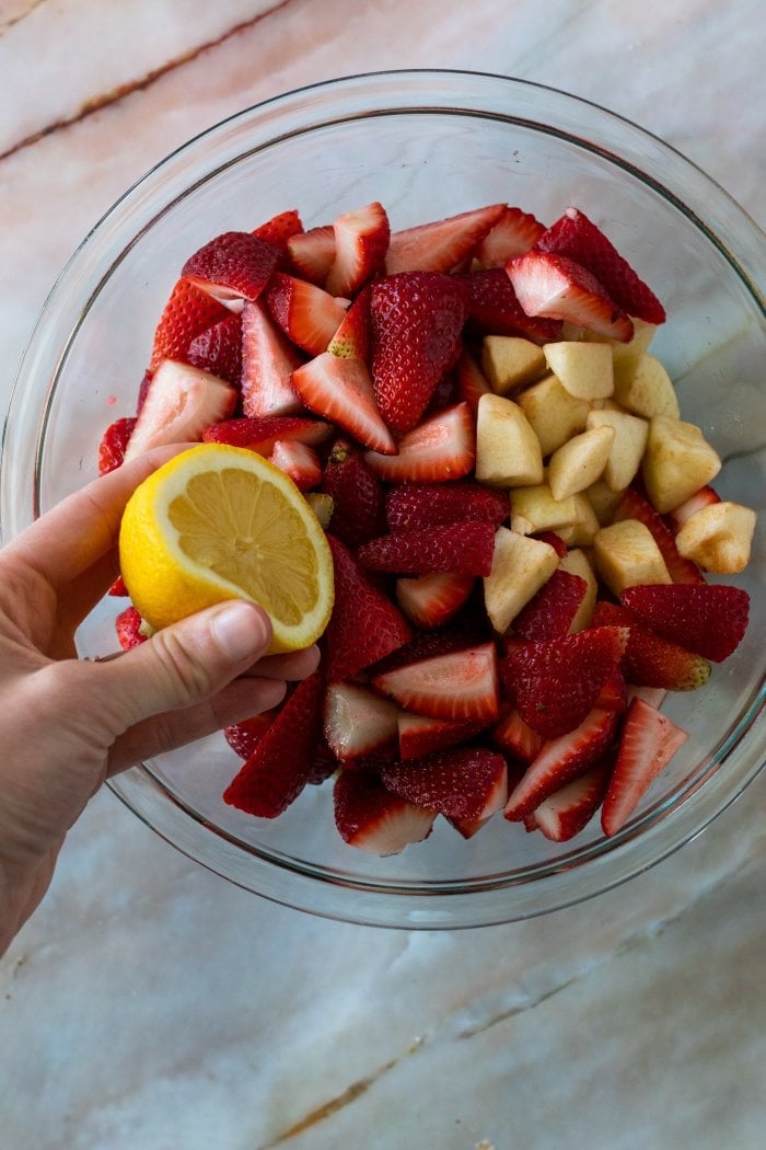 lemon is squeezed into a bowl containing strawberries and apples