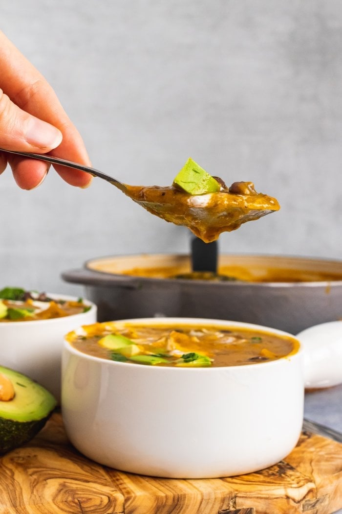 a hand lifts a spoon of black bean butternut squahsh soup out of the soup bowl resting on top of a wooden board