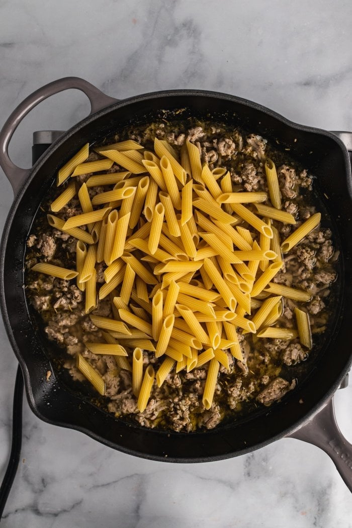 raw noodles are shown on top of turkey in a large skillet