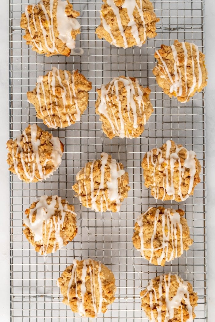 peach cobbler muffins are shown on a cooling rack topped with glaze