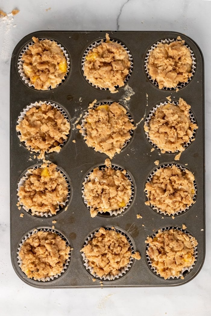 a muffin tray is filled with peach cobbler muffin batter and topped with streusel topping