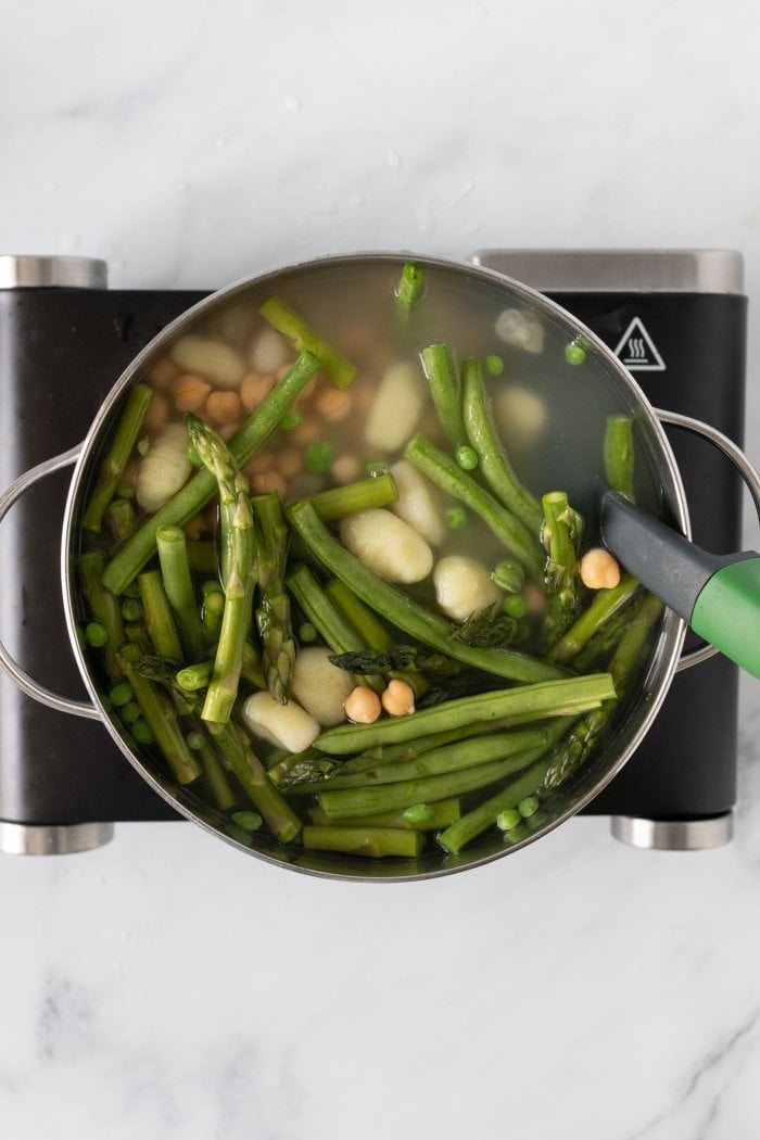 gnocchi is cooked in a large pot of water along with peas, green beans, asparagus, and