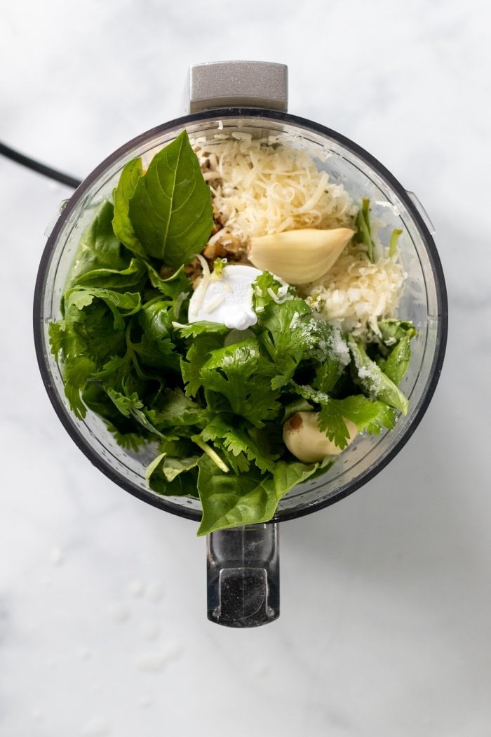 a top down view of all the ingredients for lemon basil pesto in a food processor