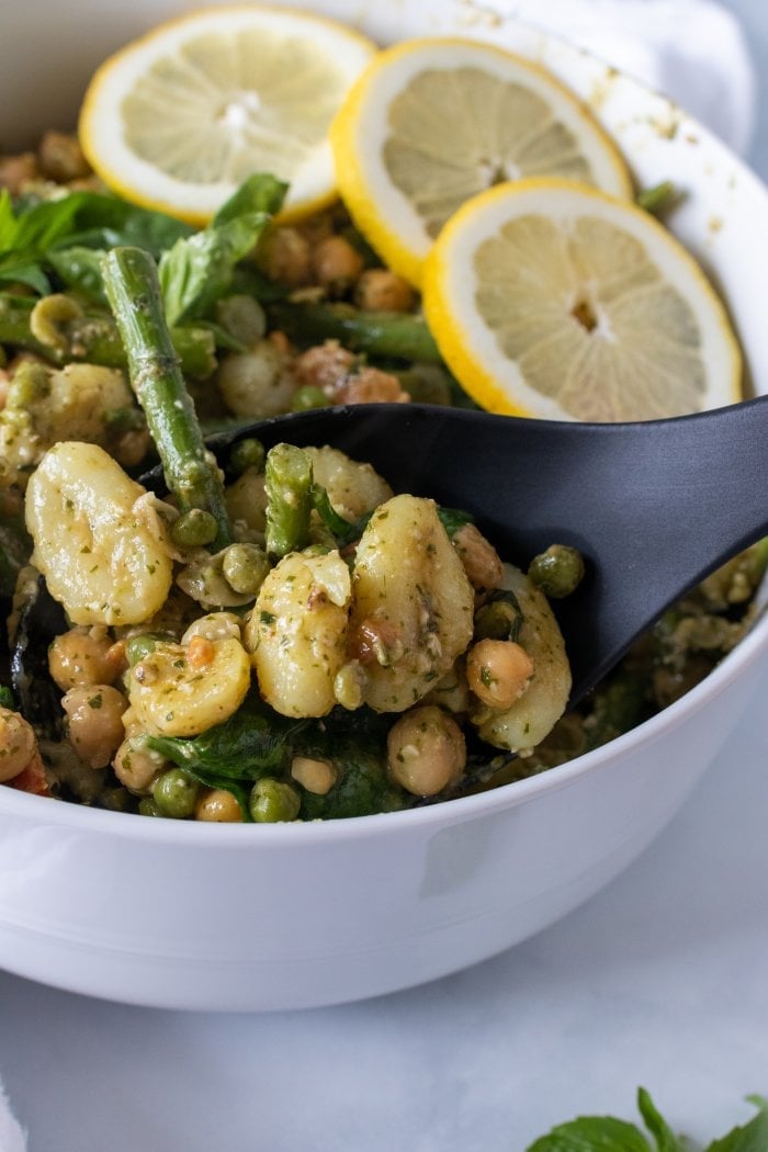 A scoop of vegetarian pesto gnocchi being scooped from the bowl