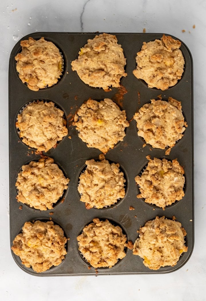 a muffin tin is shown with cooked peach cobbler muffins